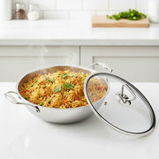 stainless steel kadai with steaming vegetable pulao and glass lid on white kitchen countertop